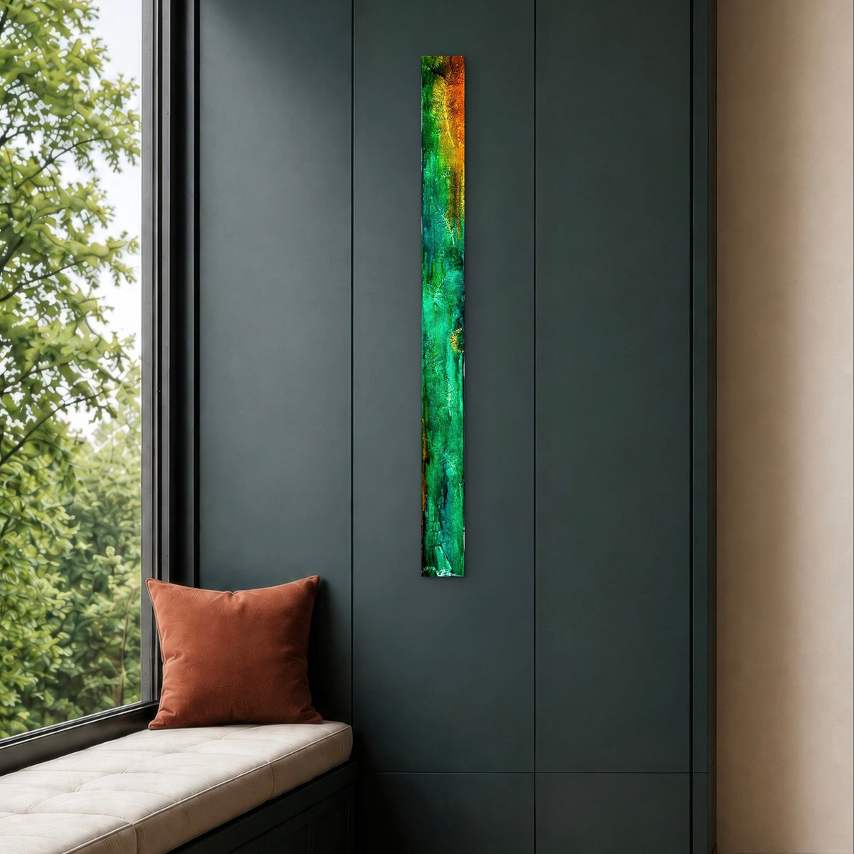 A tall, narrow abstract wall art piece with vertical streaks of green, teal, orange, and yellow mounted on a dark charcoal paneled wall next to a window with a cushioned seat and an orange pillow.
